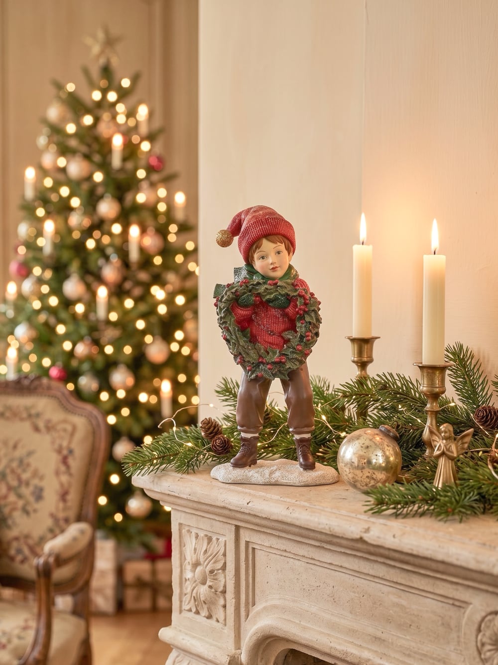Figurine petit garçon de Noël en rouge et vert tenant une couronne végétale à baies rouges, décoration de Noël poétique et féérique
