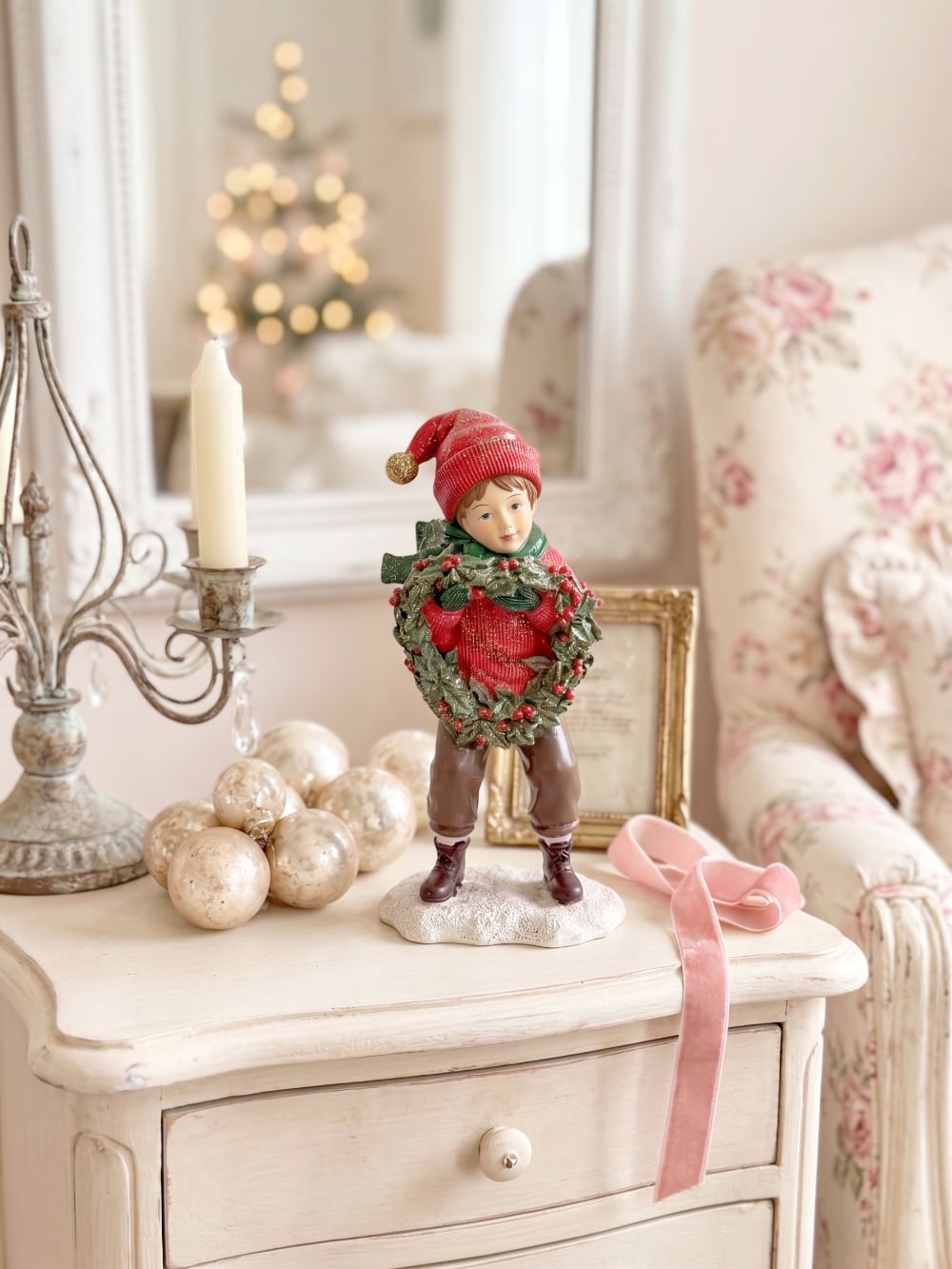 Figurine petit garçon de Noël en rouge et vert tenant une couronne végétale à baies rouges, décoration de Noël poétique et féérique