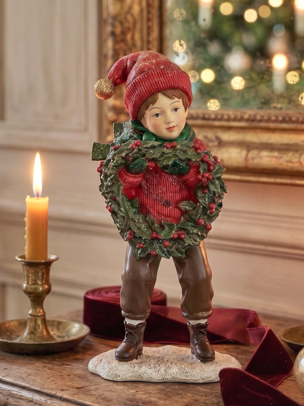 Figurine petit garçon de Noël en rouge et vert tenant une couronne végétale à baies rouges, décoration de Noël poétique et féérique