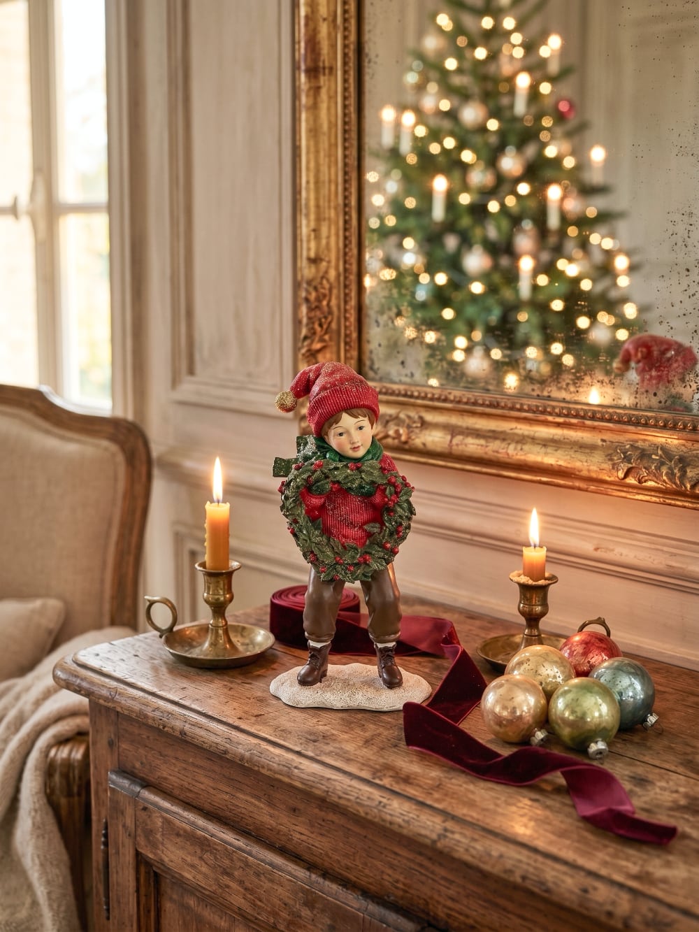 Figurine petit garçon de Noël en rouge et vert tenant une couronne végétale à baies rouges, décoration de Noël poétique et féérique