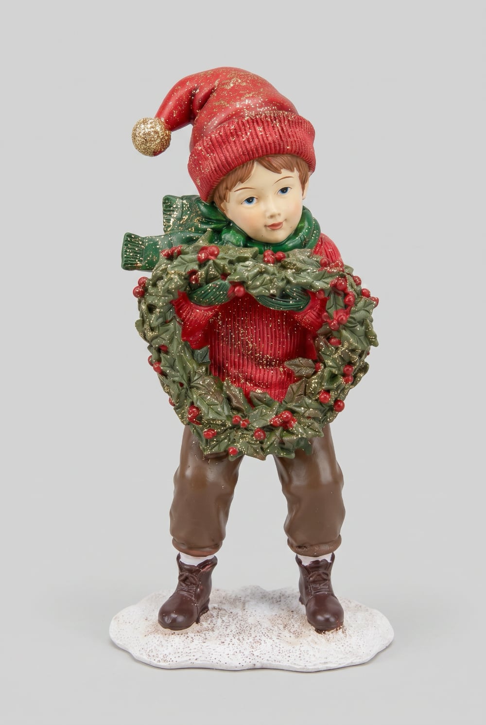 Figurine petit garçon de Noël en rouge et vert tenant une couronne végétale à baies rouges, décoration de Noël poétique et féérique