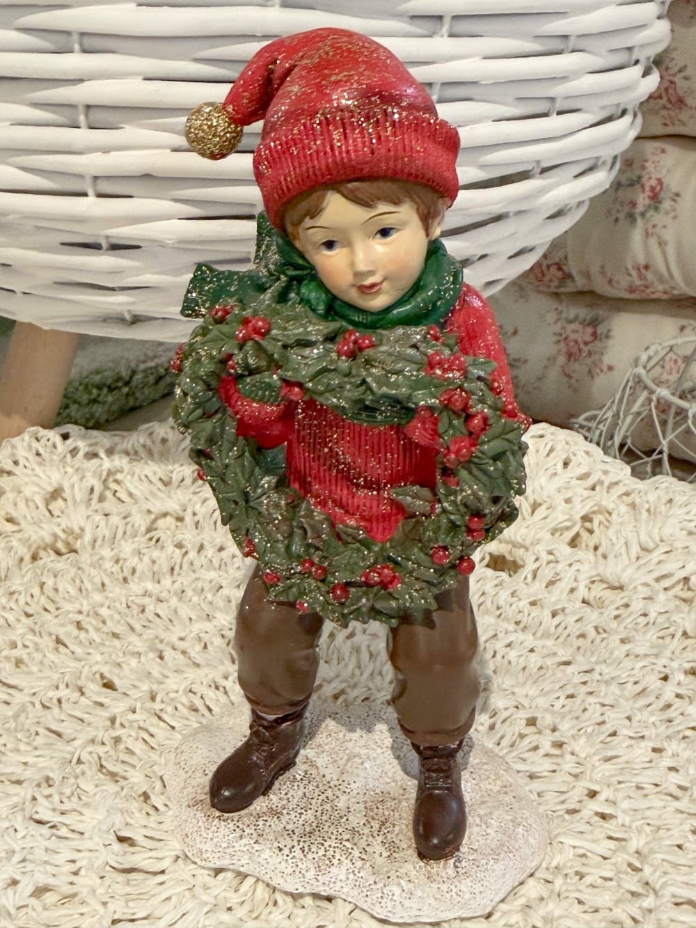 Figurine petit garçon de Noël en rouge et vert tenant une couronne végétale à baies rouges, décoration de Noël poétique et féérique