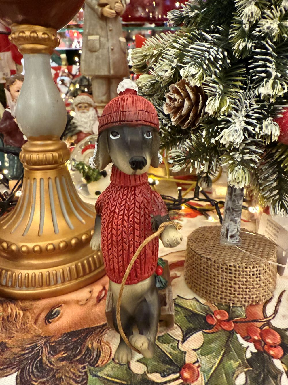 Figurine de teckel des neiges en pull rouge avec bonnet, accompagnée d’une luge et d’un petit sapin, style déco de Noël shabby chic et féérique