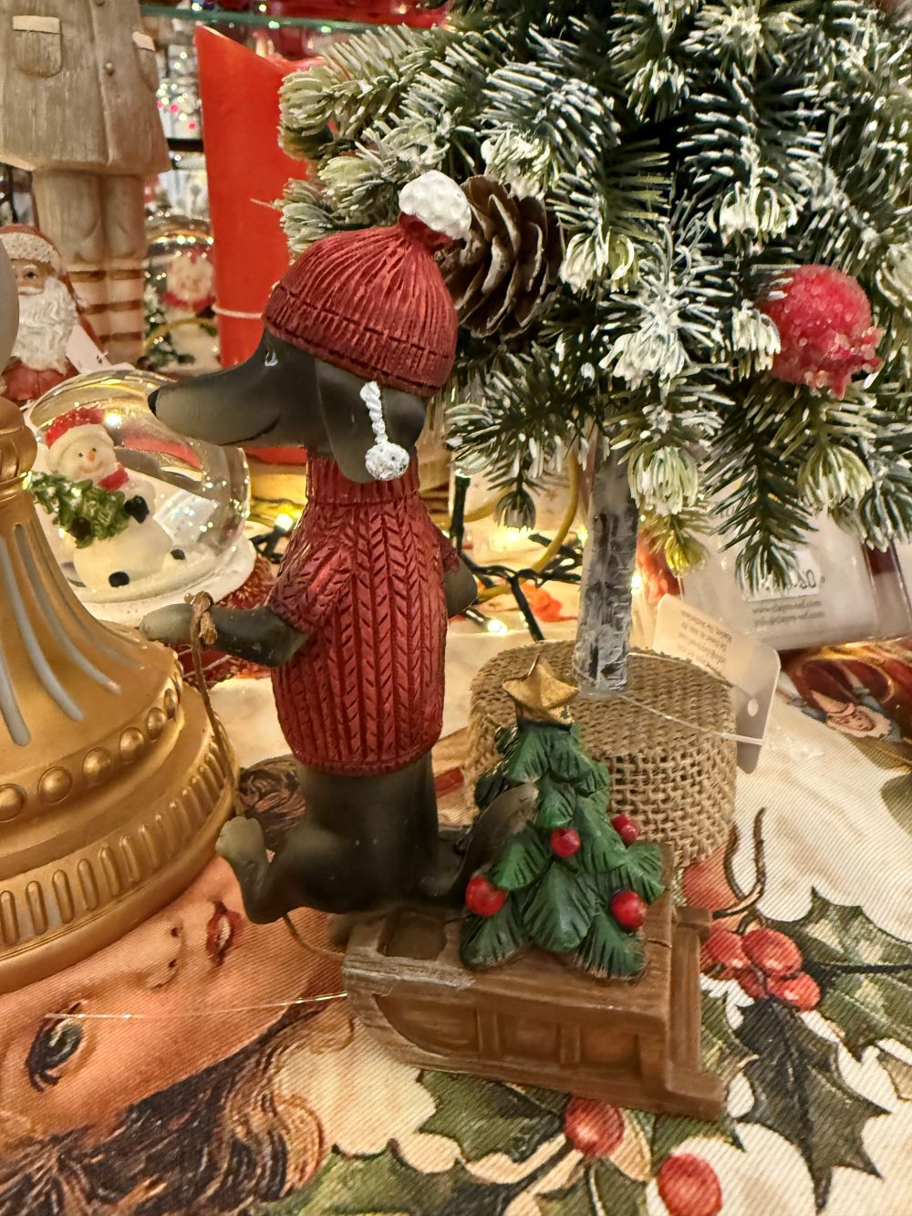 Figurine de teckel des neiges en pull rouge avec bonnet, accompagnée d’une luge et d’un petit sapin, style déco de Noël shabby chic et féérique