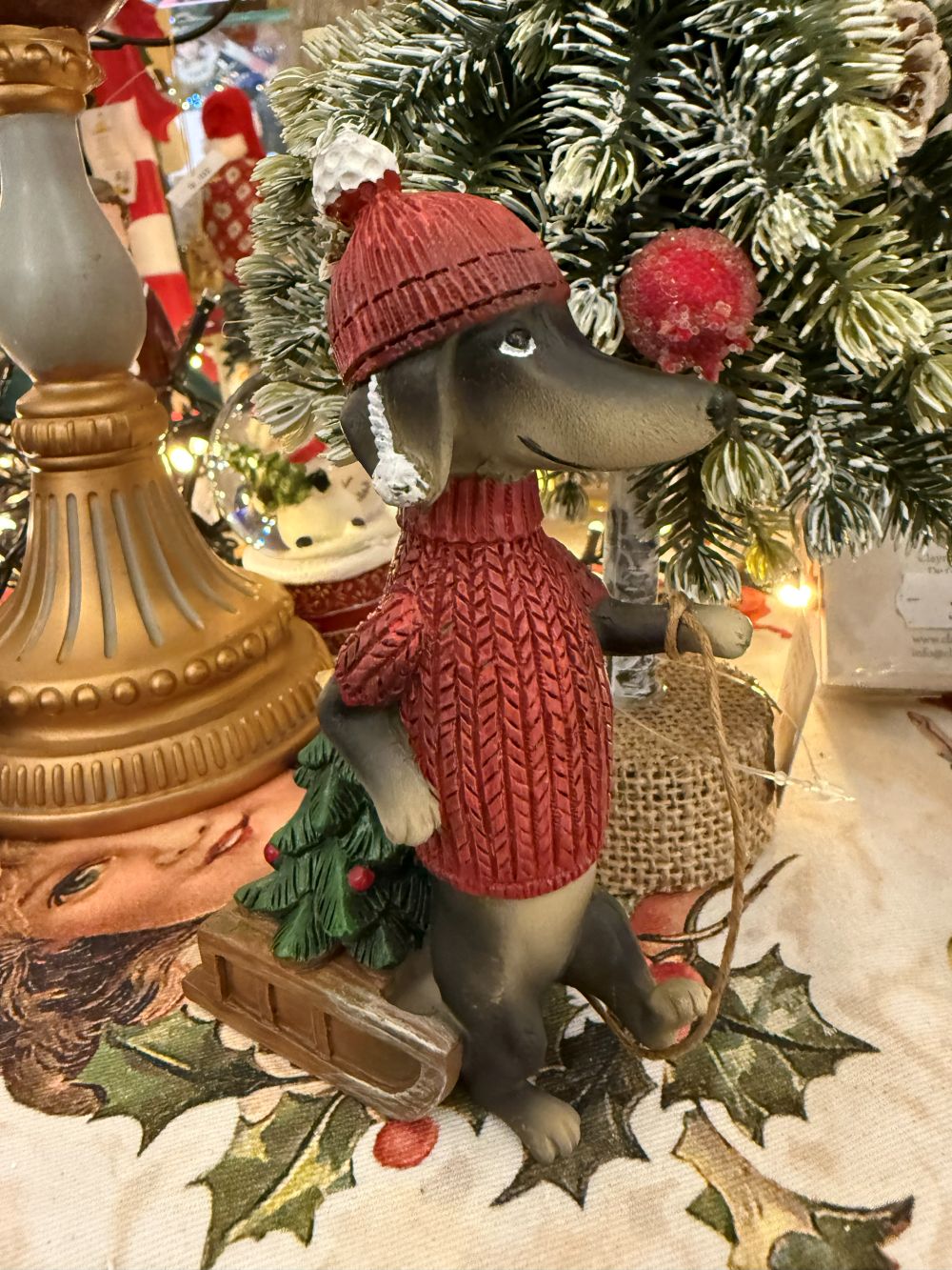 Figurine de teckel des neiges en pull rouge avec bonnet, accompagnée d’une luge et d’un petit sapin, style déco de Noël shabby chic et féérique