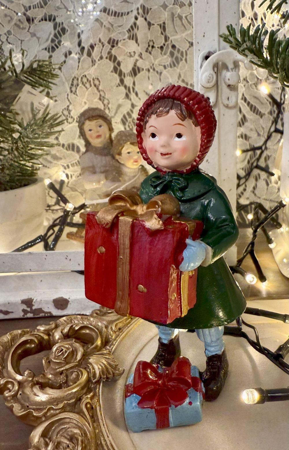 Figurine de Noël représentant une petite fille en manteau vert et bonnet rouge tenant des cadeaux, style vintage et ambiance romantique, décoration poétique pour fêtes de fin d’année