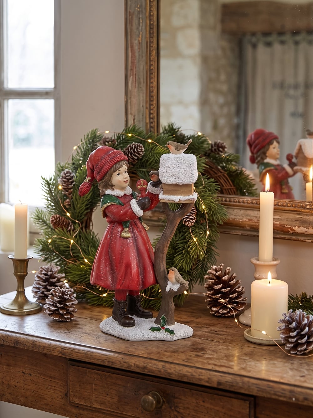 Figurine représentant une fillette en manteau rouge nourrissant des rouge-gorges près d'un nichoir enneigé, décoration de Noël romantique et poétique