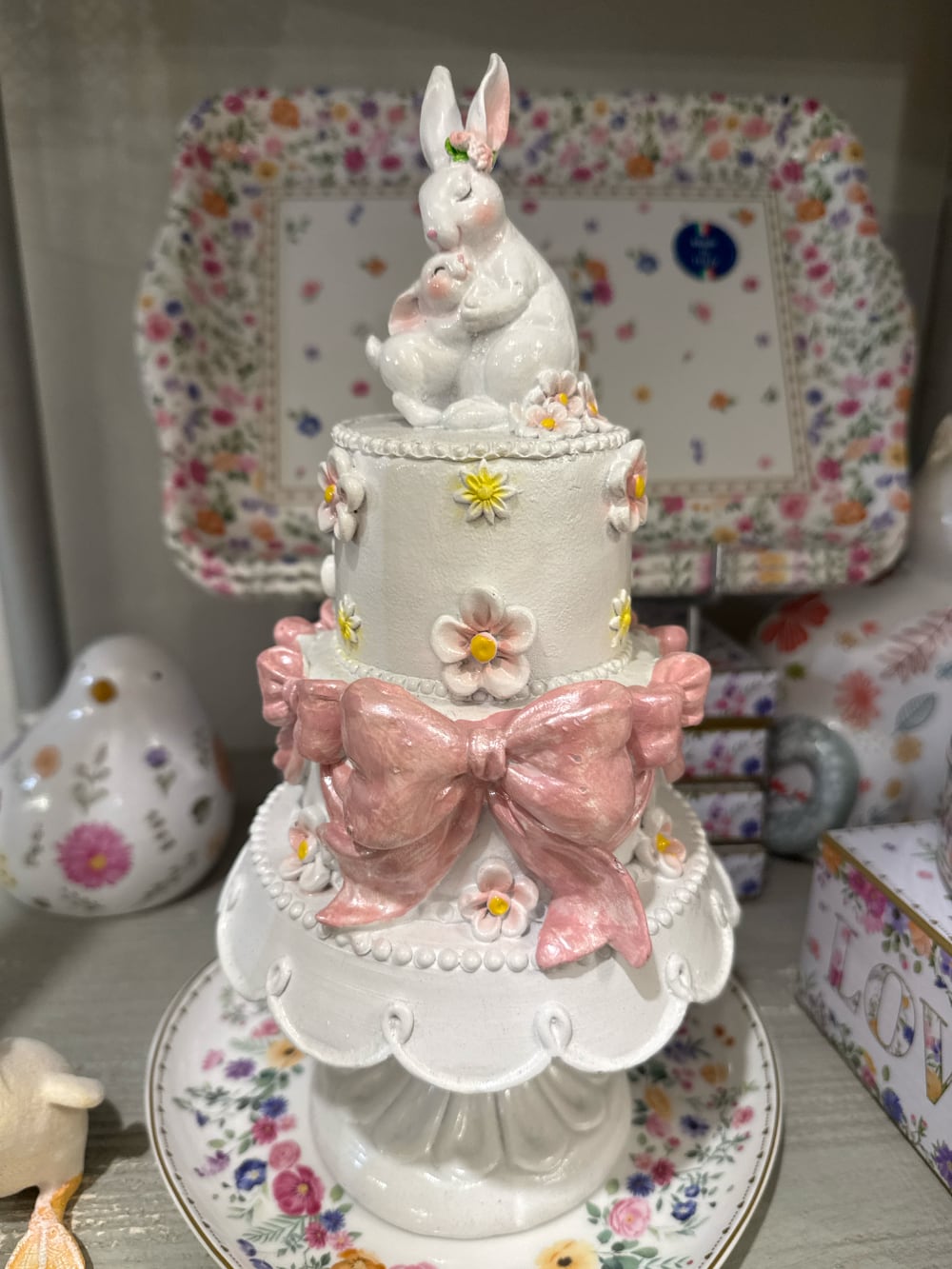 Gâteau décoratif à étages orné de fleurs pastel et de grands nœuds rose poudré avec une maman lapin et son petit au sommet, décoration romantique de Pâques et ambiance féérique