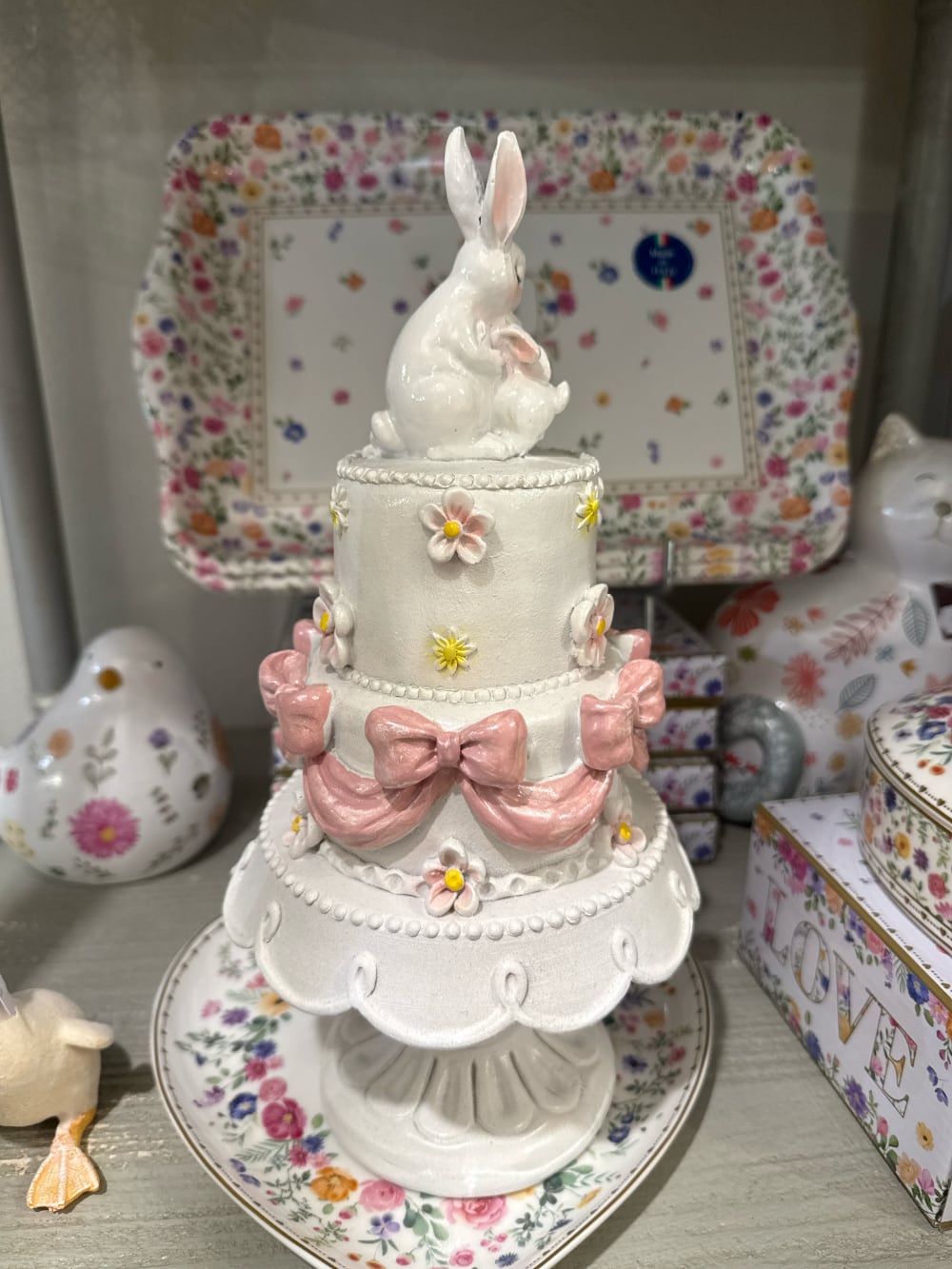 Gâteau décoratif à étages orné de fleurs pastel et de grands nœuds rose poudré avec une maman lapin et son petit au sommet, décoration romantique de Pâques et ambiance féérique
