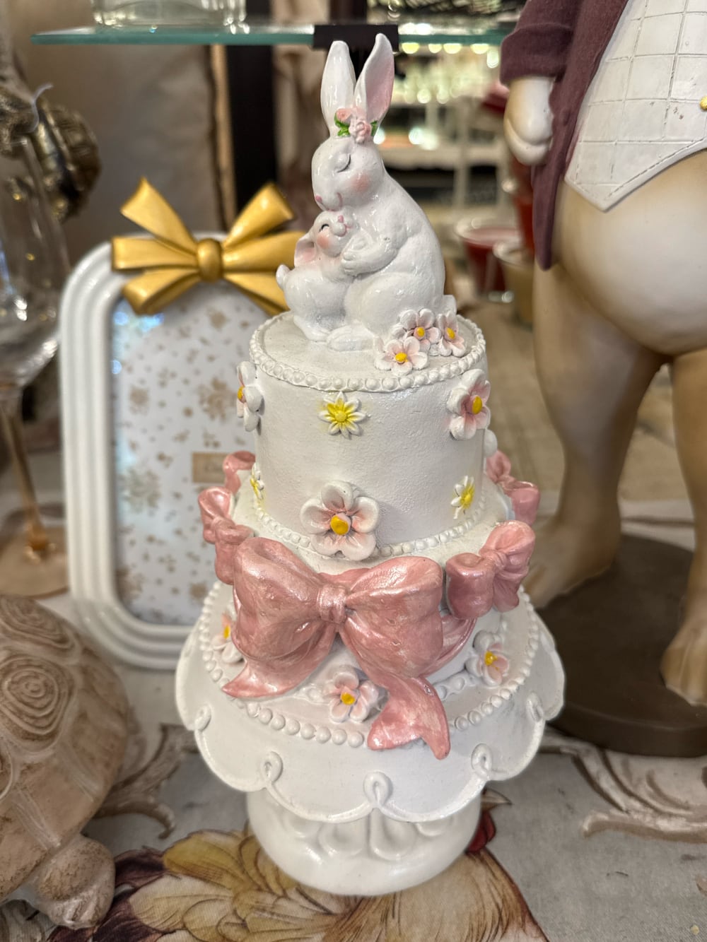 Gâteau décoratif à étages orné de fleurs pastel et de grands nœuds rose poudré avec une maman lapin et son petit au sommet, décoration romantique de Pâques et ambiance féérique