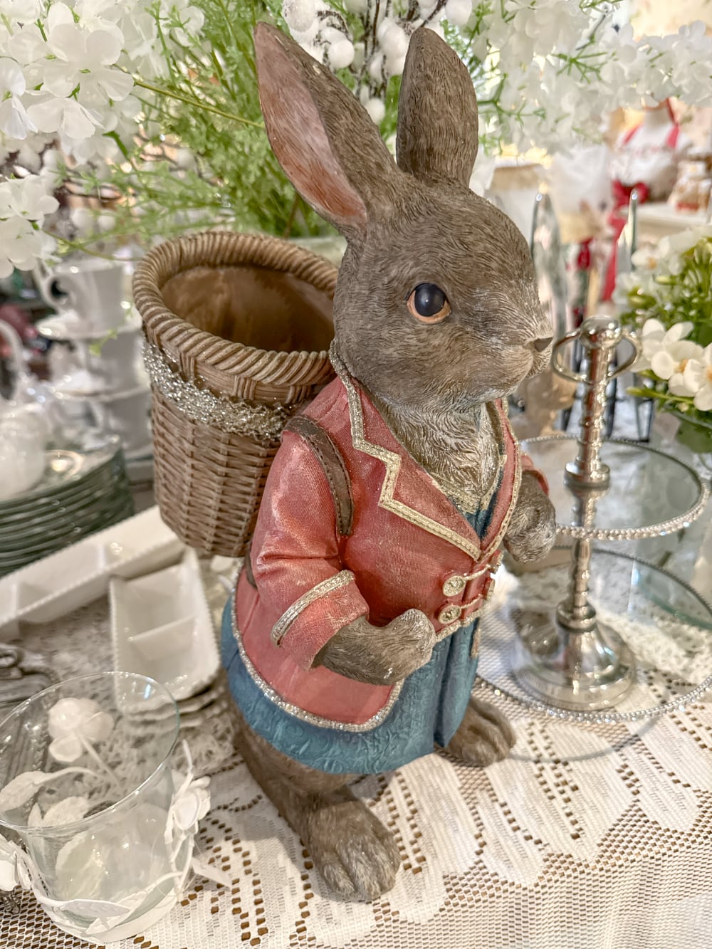 Grand lapin décoratif brun vêtu de rose et bleu avec panier dans le dos, style Alice romantique et décoration poétique de Pâques