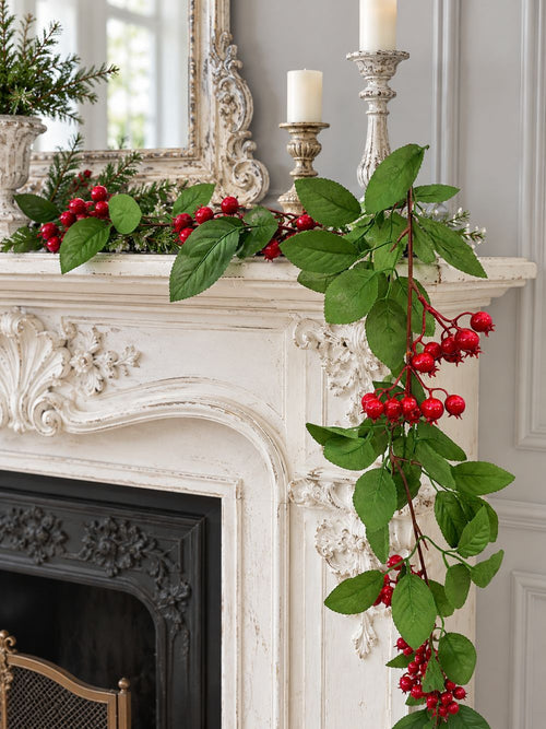 Guirlande de baies rouges et de feuilles vertes disposée sur une cheminée ancienne blanc patiné.