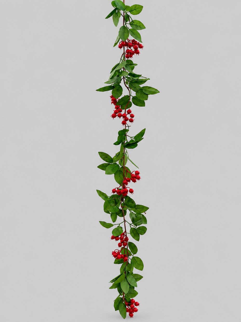 Guirlande artificielle de baies rouges et de feuilles vertes, suspendue sur fond gris clair.