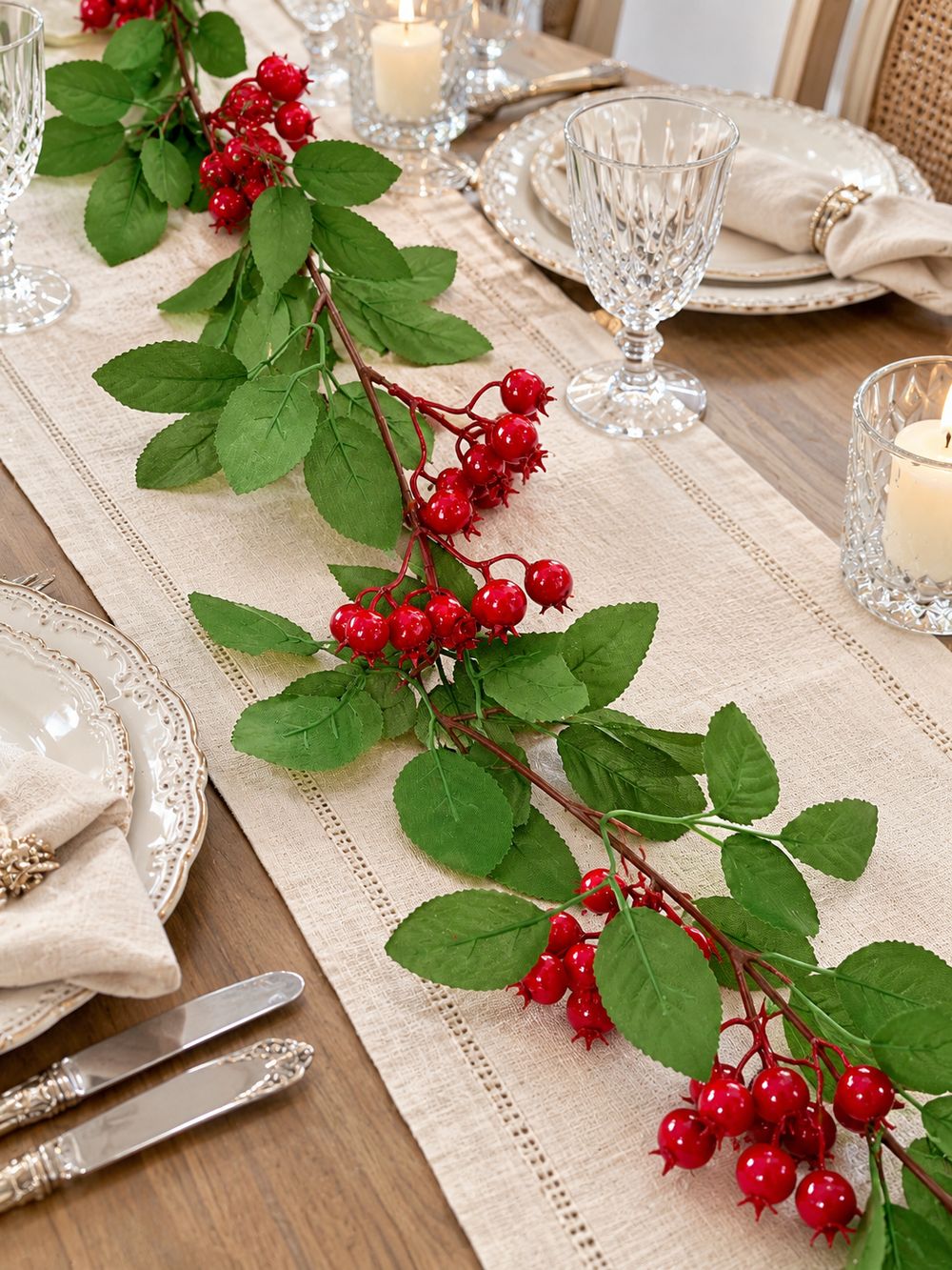 Guirlande de baies rouges sur un chemin de table en lin, entourée de vaisselle blanche et de verres transparents.
