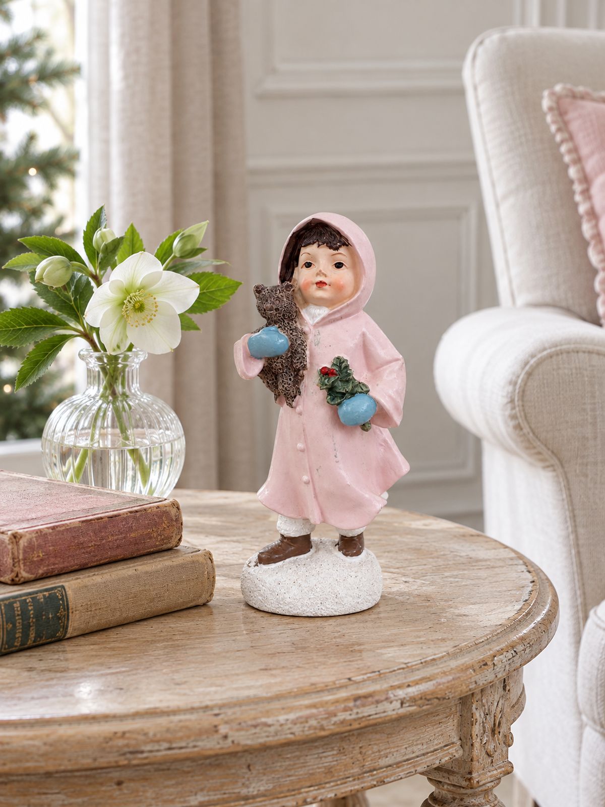 Figurine Héloïse et son ourson sur un guéridon en bois, avec des livres anciens et des hellébores blanches.