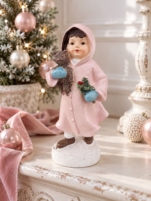 Figurine Héloïse et son ourson sur une console patinée, près d’un sapin décoré de boules roses et nacrées.