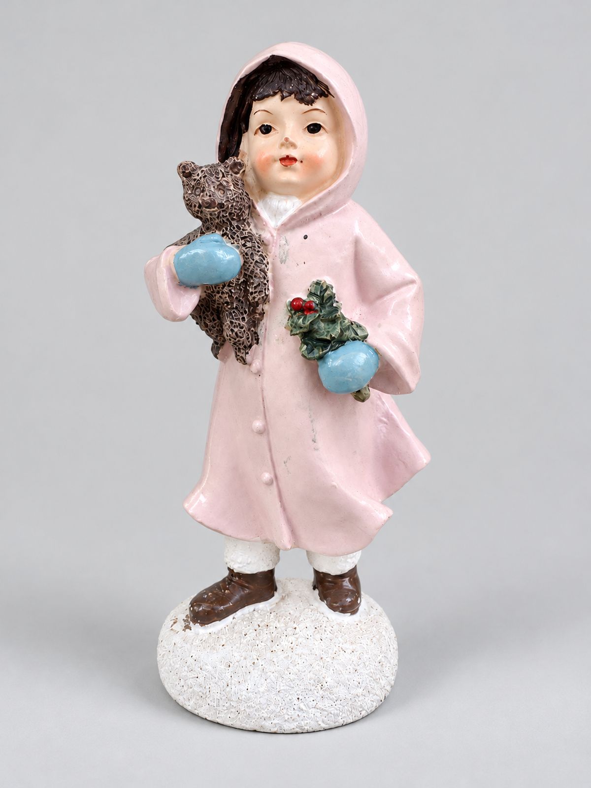 Figurine Héloïse en manteau rose et moufles bleues, tenant son ourson et un brin de houx, sur fond gris clair.