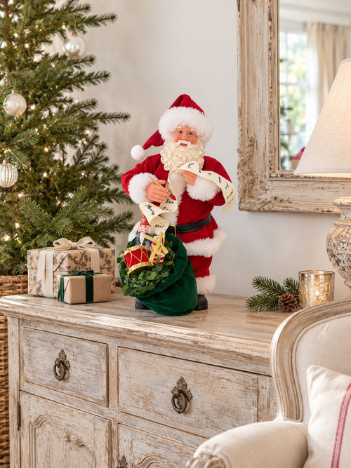 Figurine La lettre au père Noël sur un buffet patiné dans un salon lumineux, avec un sapin décoré et de petits cadeaux.
