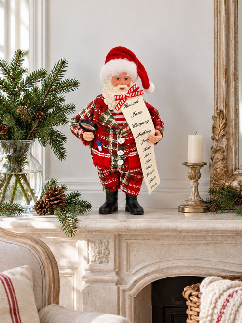 Figurine Père Noël sur une cheminée en pierre claire, entourée de branches de sapin et d’un bougeoir.