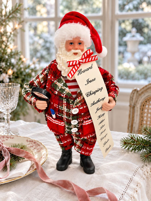 Figurine Père Noël avec sa liste sur une table de fête en lin blanc, près d’une fenêtre.