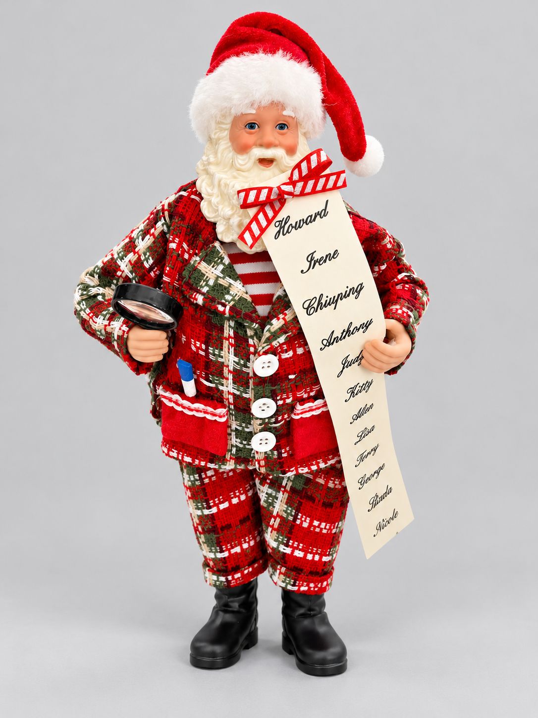 Figurine Père Noël en costume à carreaux rouges et verts, tenant une liste et une loupe, sur fond gris clair.