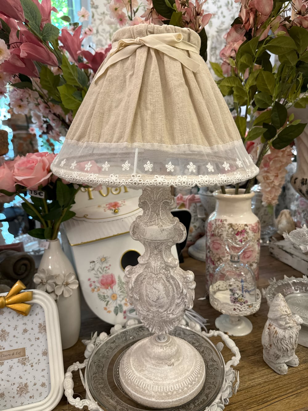Lampe de table romantique avec pied sculpté blanc patiné et abat-jour en tissu naturel orné de dentelle blanche, idéale pour une décoration shabby chic et de charme