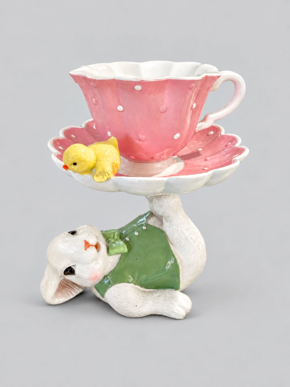 Figurine décorative avec lapin blanc vêtu de vert portant une grande tasse rose à pois, soucoupe fleurie et petit poussin jaune, ambiance de Pâques féérique