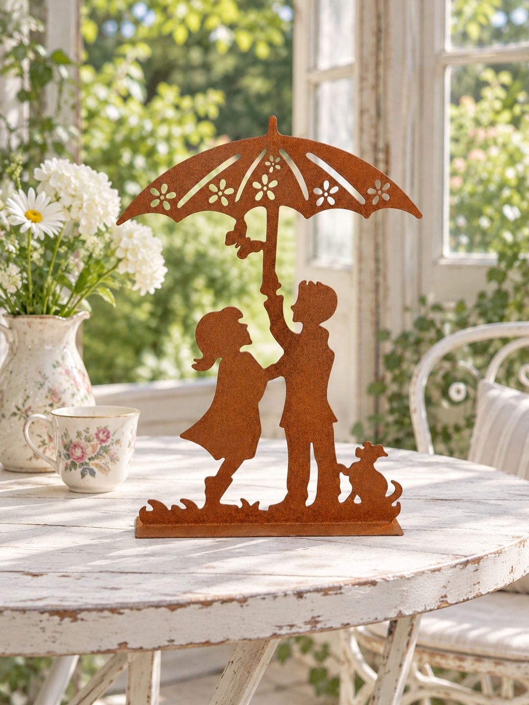 Décoration Les Amoureux au Jardin sur une table blanche patinée dans une véranda lumineuse, près d’une tasse fleurie.