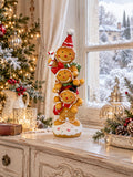 Figurine décorative de Noël composée de trois petits personnages façon pain d’épices superposés, aux tons caramel, rouge, vert et blanc, pour une décoration festive et féérique.