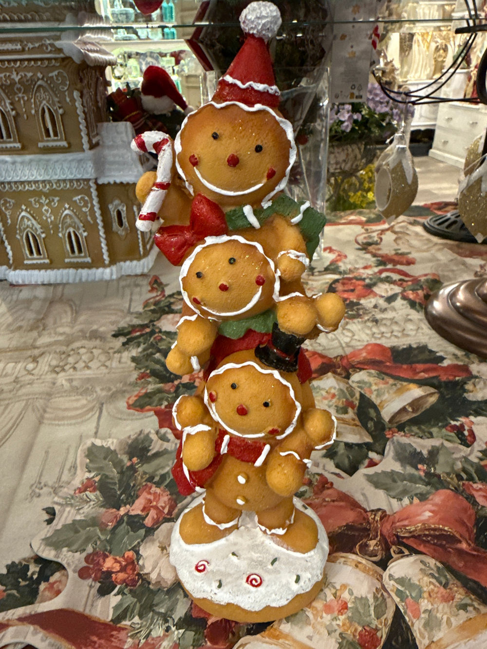 Figurine décorative de Noël composée de trois petits personnages façon pain d’épices superposés, aux tons caramel, rouge, vert et blanc, pour une décoration festive et féérique.