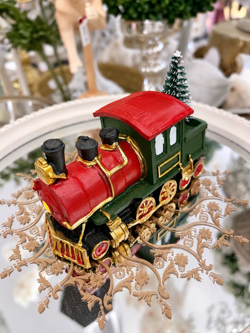 Locomotive décorative de Noël rouge et verte avec détails dorés et sapin enneigé, vue de trois quarts.