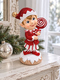 Lutin rouge pailleté sur une console blanche patinée près d’une fenêtre, accompagné de branches de sapin et d’une boule argentée.