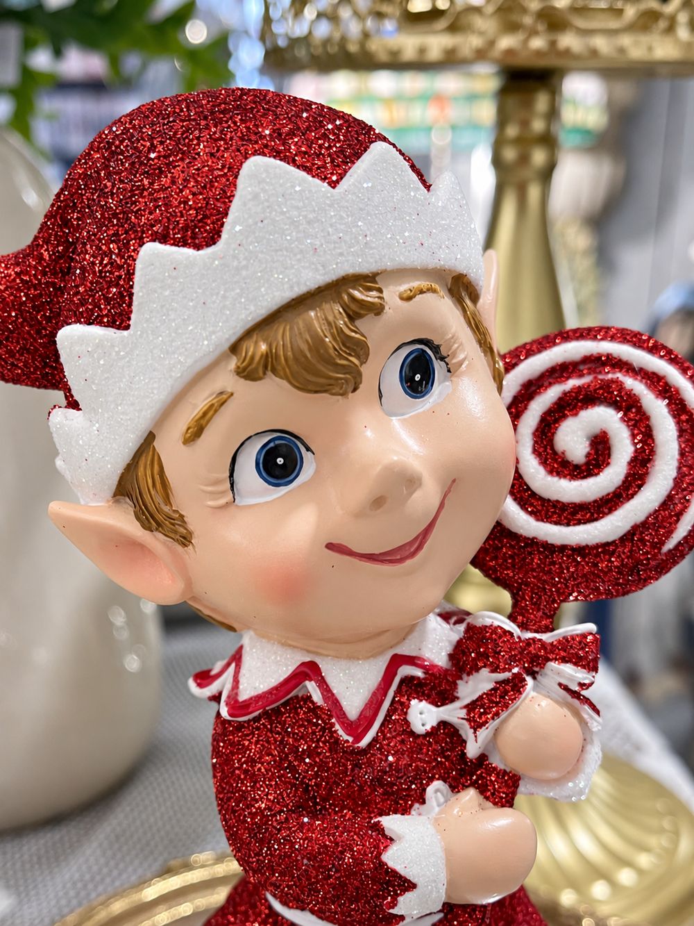 Gros plan du visage souriant du lutin pailleté, de son bonnet rouge et de sa sucette en spirale.