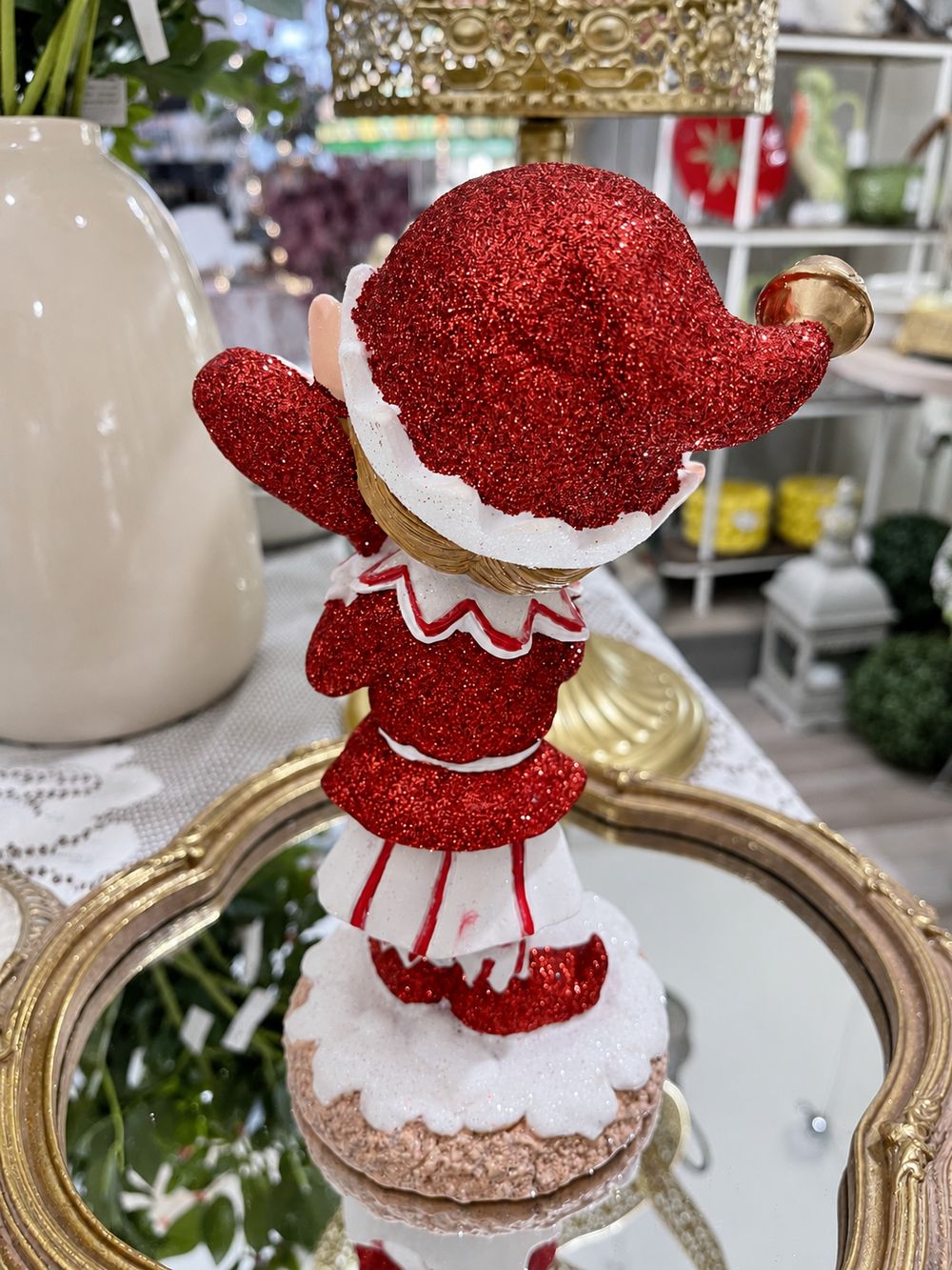 Vue de dos du lutin rouge pailleté, montrant son bonnet à grelot doré et son costume rouge et blanc.