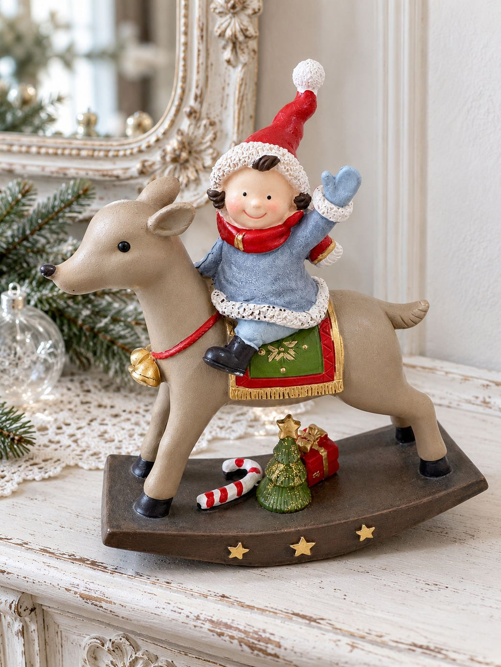 Figurine de lutin à dos de renne sur une console blanche patinée, devant un miroir ancien et quelques branches de sapin.