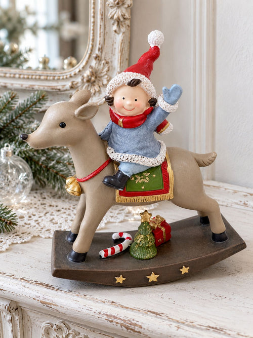 Figurine de lutin à dos de renne sur une console blanche patinée, devant un miroir ancien et quelques branches de sapin.