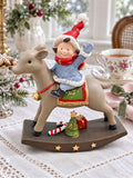 Figurine de lutin à dos de renne sur une table de Noël en lin blanc, près d’une tasse fleurie et d’une serviette rose.