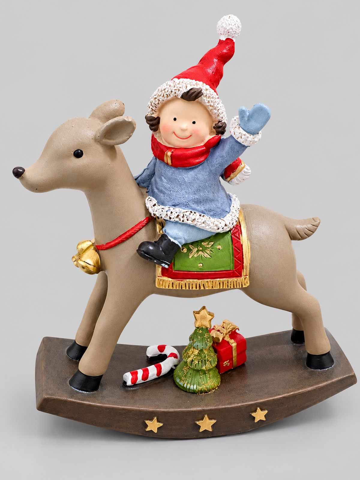 Figurine de Noël représentant un lutin au bonnet rouge chevauchant un renne, sur un socle étoilé, sur fond gris clair.