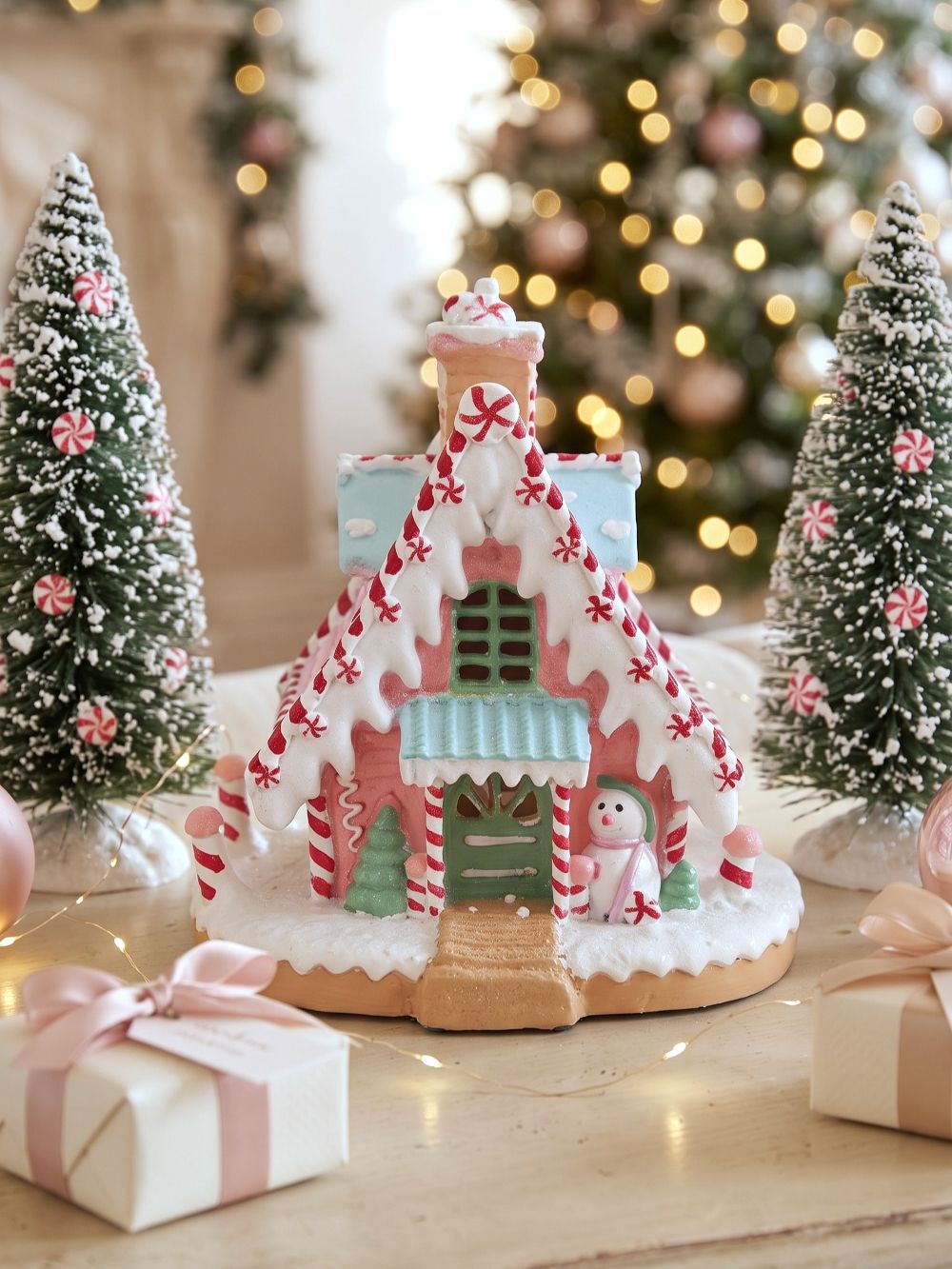 Maisonnette pain d’épice décorative de Noël rose pastel, blanche et bleu ciel, avec décor enneigé et bonhomme de neige, pour ambiance de Noël féérique