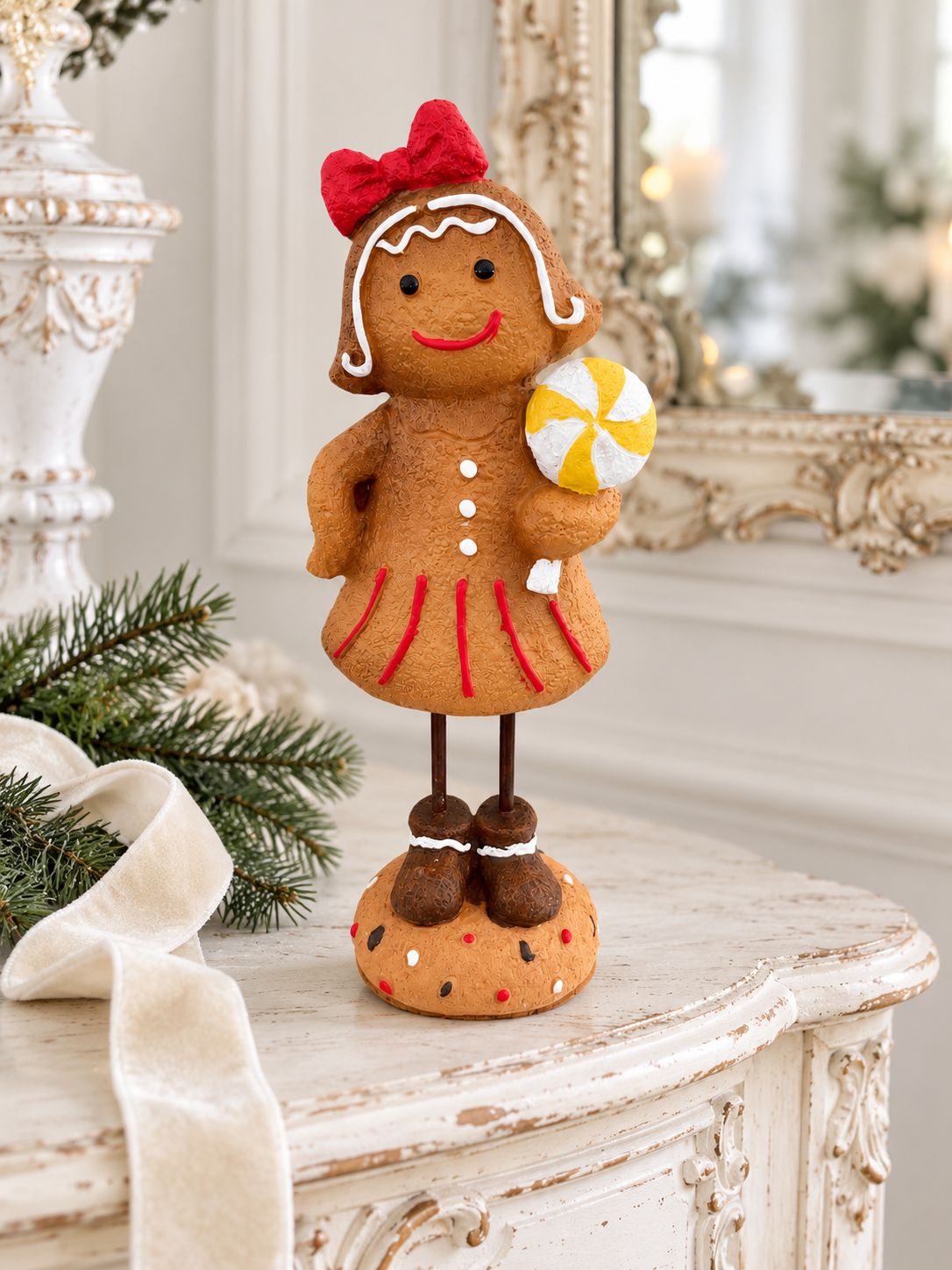 Figurine Mme Gingerman sur une console blanche patinée, près d’une branche de sapin et d’un ruban ivoire.