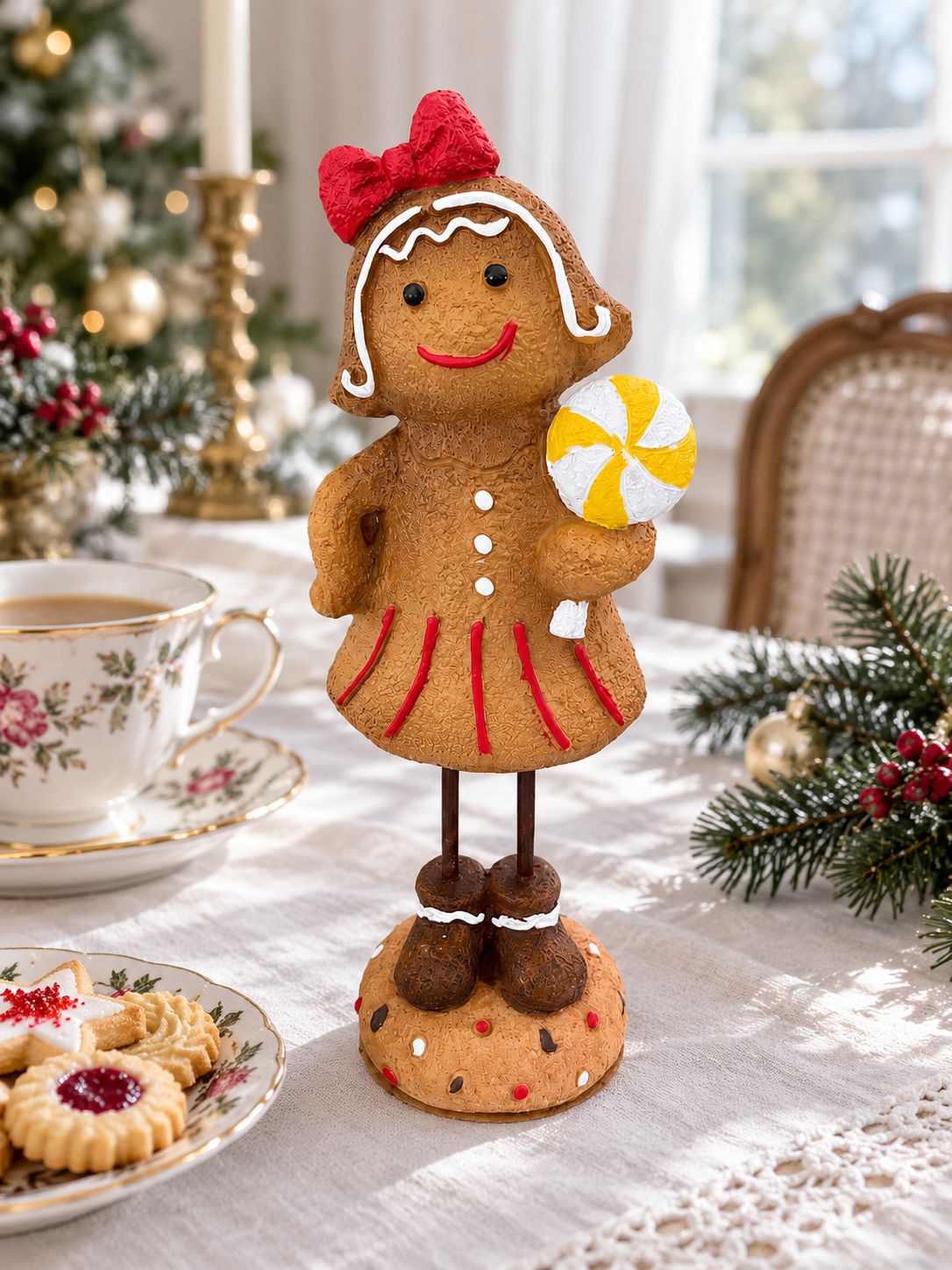 Figurine Mme Gingerman sur une table de goûter de Noël, accompagnée d’une tasse fleurie et de biscuits.