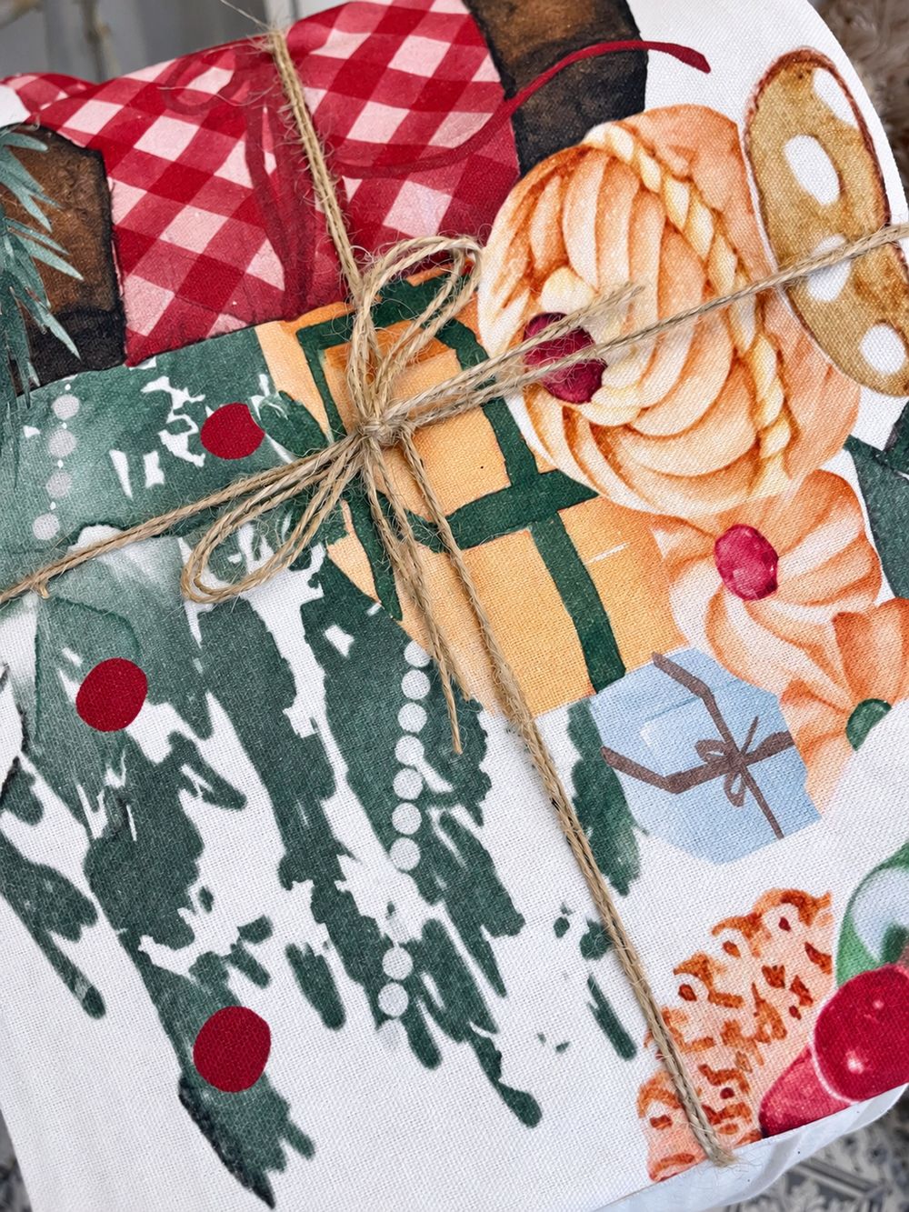Détail du coton et des motifs de la nappe Gourmandises de Noël pliée et liée avec une ficelle.