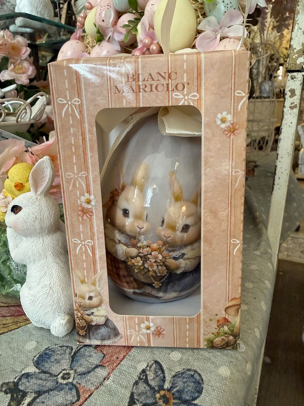 Œuf décoratif romantique Blanc Mariclò avec illustration de lapins tenant des fleurs, tons blanc beige et rose poudré, ambiance shabby chic et décoration de charme printanière