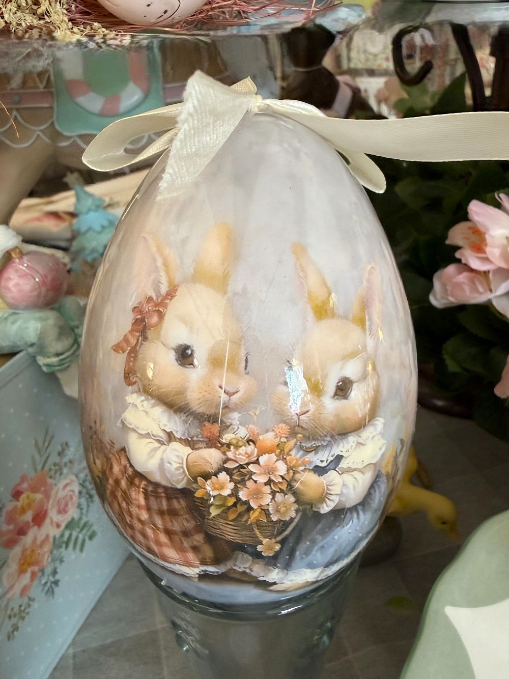 Œuf décoratif romantique Blanc Mariclò avec illustration de lapins tenant des fleurs, tons blanc beige et rose poudré, ambiance shabby chic et décoration de charme printanière