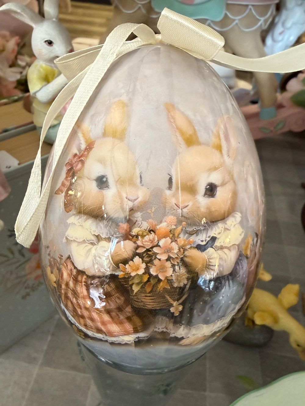 Œuf décoratif romantique Blanc Mariclò avec illustration de lapins tenant des fleurs, tons blanc beige et rose poudré, ambiance shabby chic et décoration de charme printanière