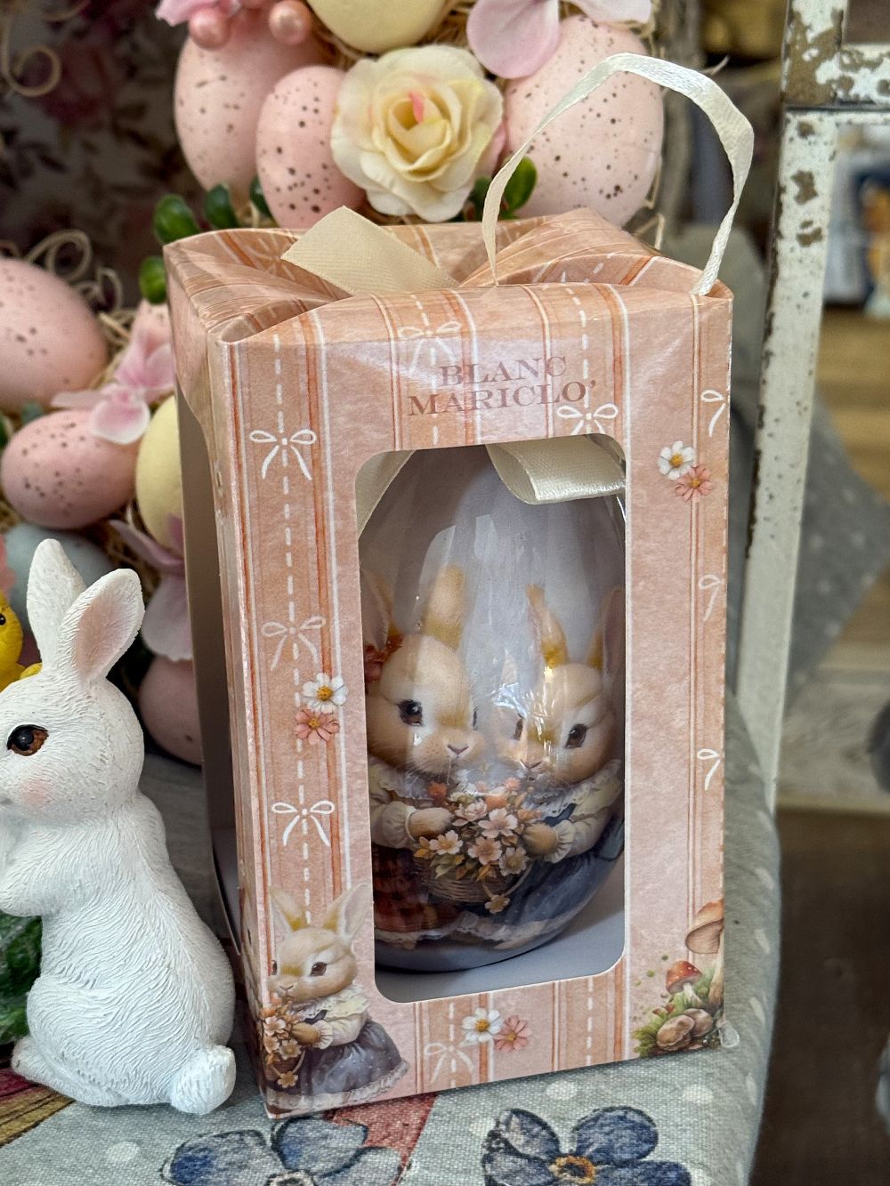 Œuf décoratif romantique Blanc Mariclò avec illustration de lapins tenant des fleurs, tons blanc beige et rose poudré, ambiance shabby chic et décoration de charme printanière