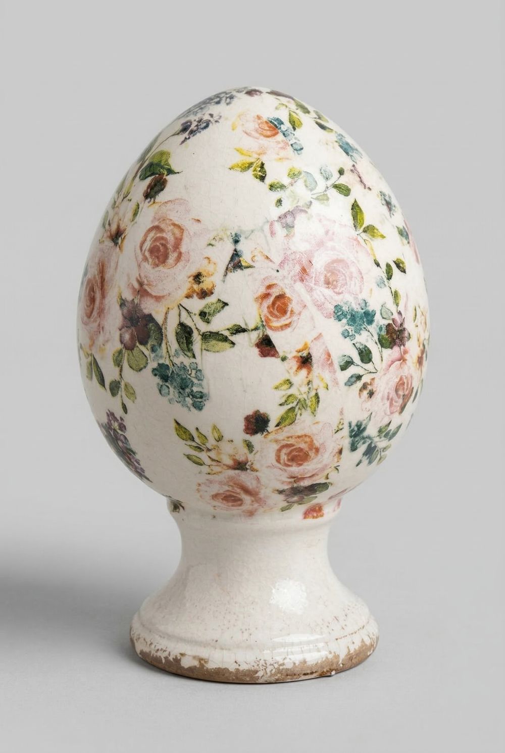 Œuf décoratif fleuri style Liberty avec roses et feuillages dans des tons rose et vert sur fond ivoire, posé sur un socle patiné, décoration romantique shabby chic pour intérieur de charme.