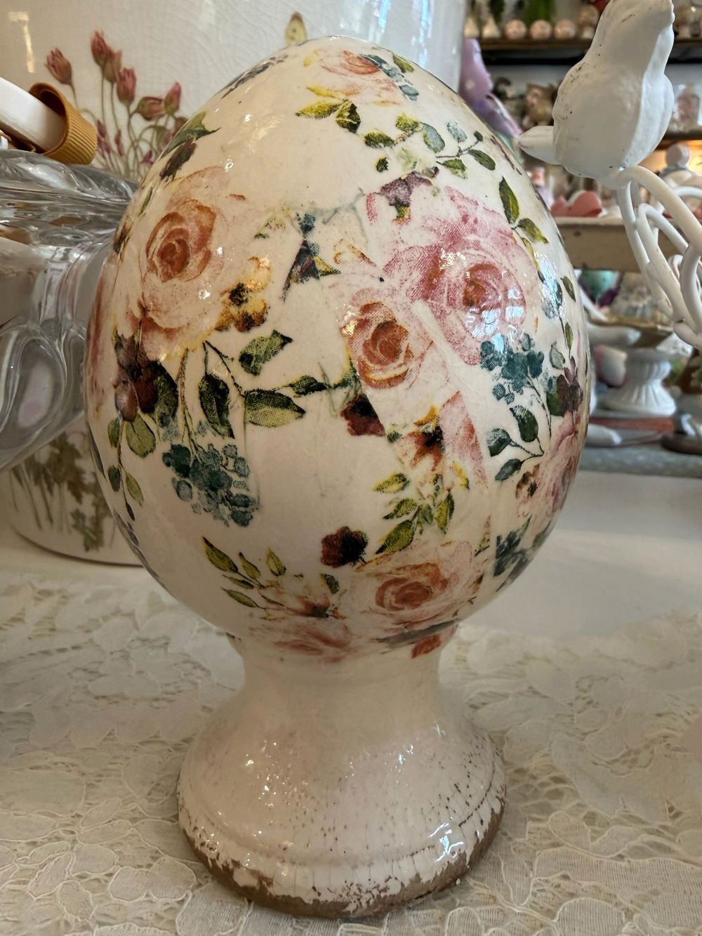 Œuf décoratif fleuri style Liberty avec roses et feuillages dans des tons rose et vert sur fond ivoire, posé sur un socle patiné, décoration romantique shabby chic pour intérieur de charme.