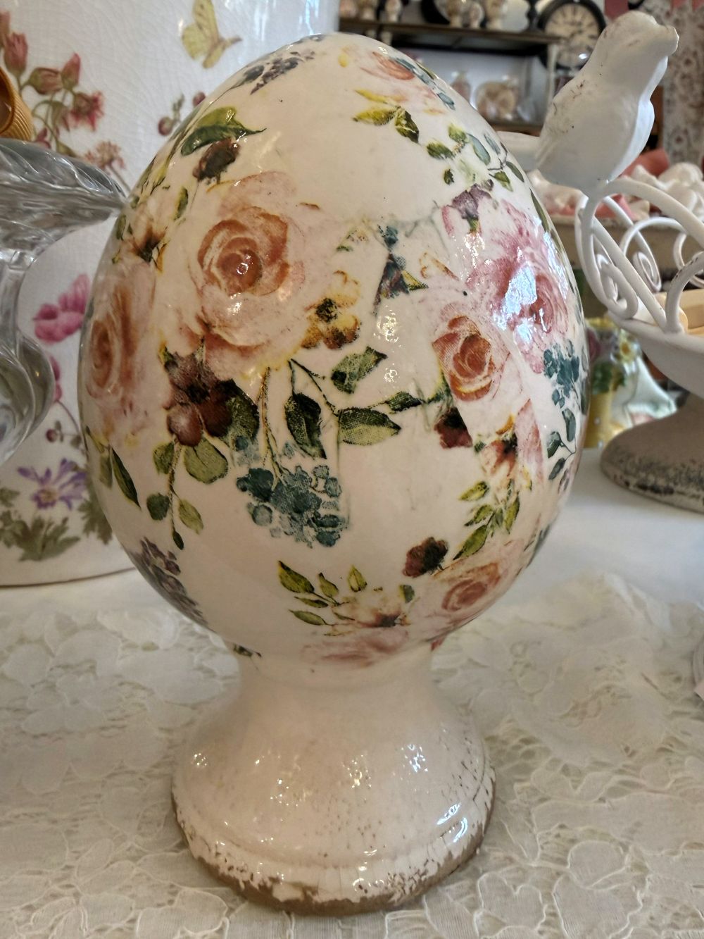 Œuf décoratif fleuri style Liberty avec roses et feuillages dans des tons rose et vert sur fond ivoire, posé sur un socle patiné, décoration romantique shabby chic pour intérieur de charme.