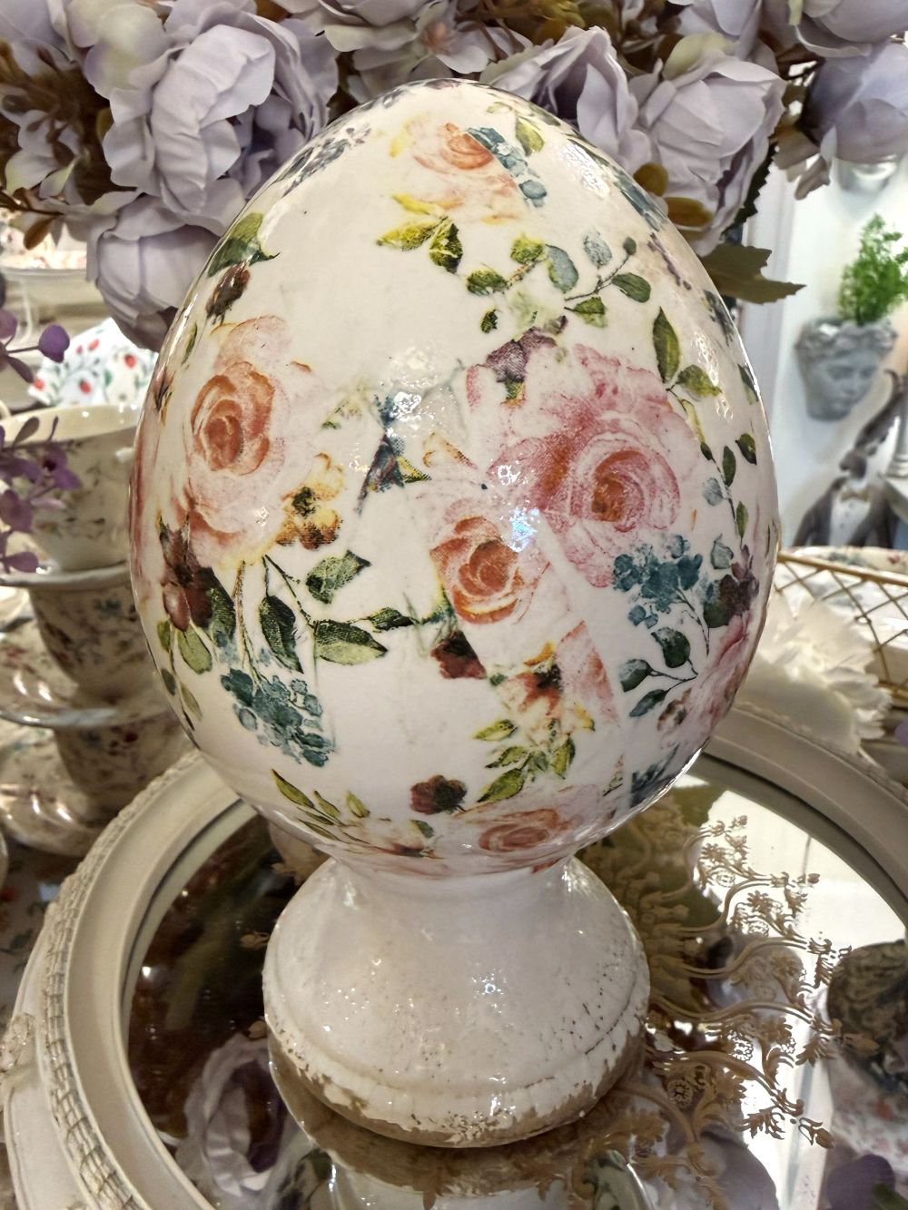 Œuf décoratif fleuri style Liberty avec roses et feuillages dans des tons rose et vert sur fond ivoire, posé sur un socle patiné, décoration romantique shabby chic pour intérieur de charme.